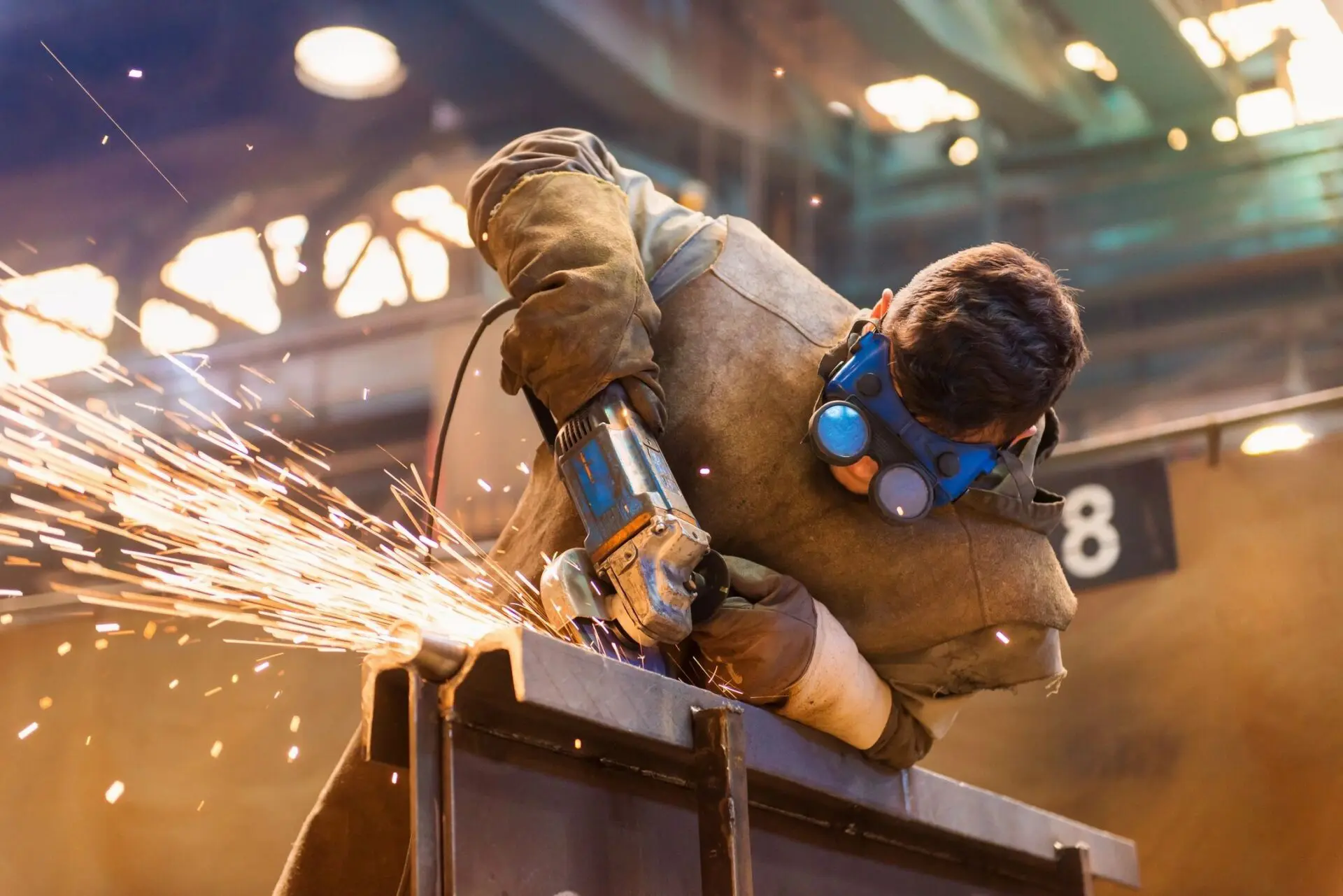 A man wearing protective gear and using an angle grinder.